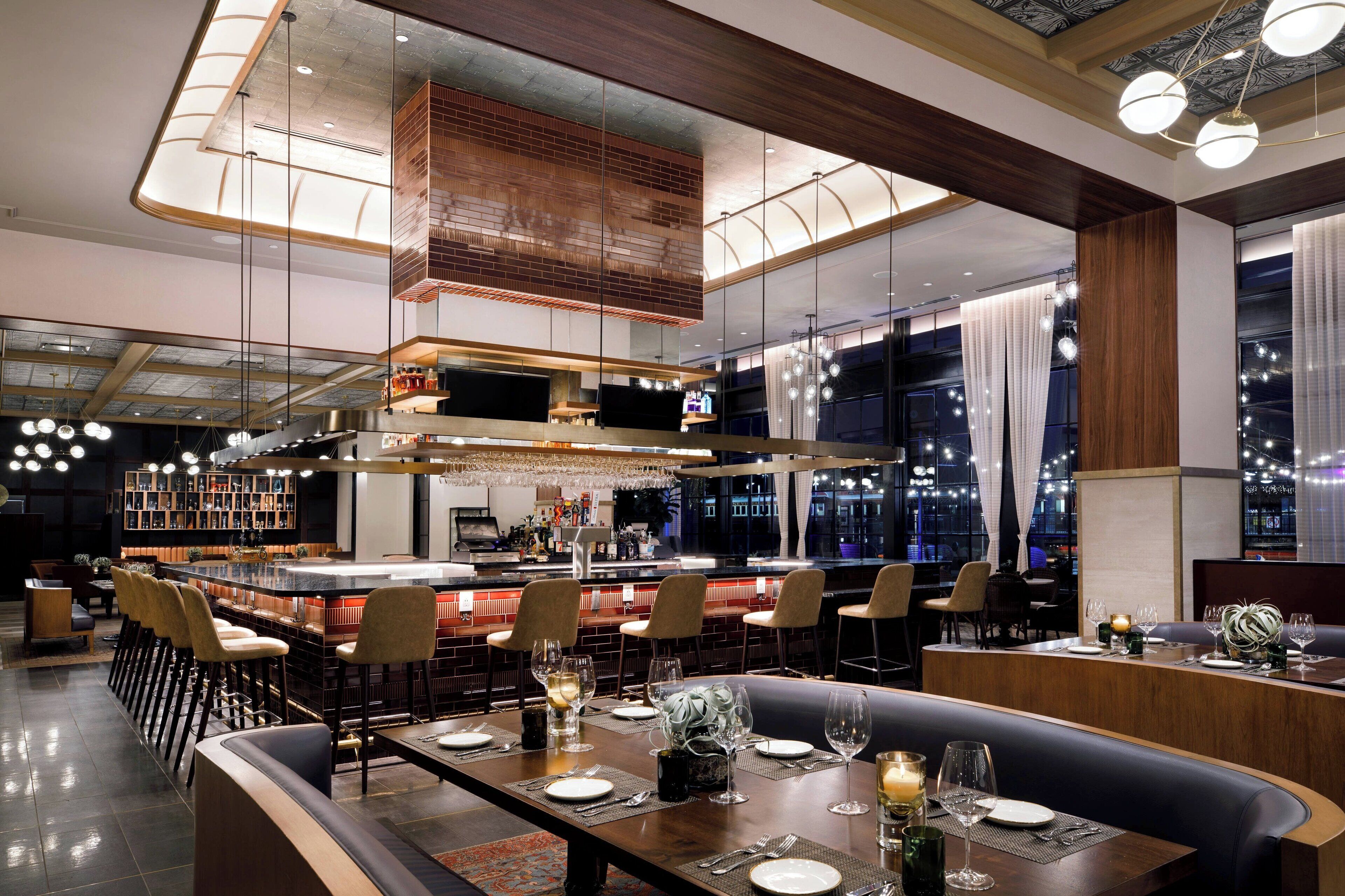 Ein modernes Restaurant mit Barbereich, hohen Decken und großen Fenstern.