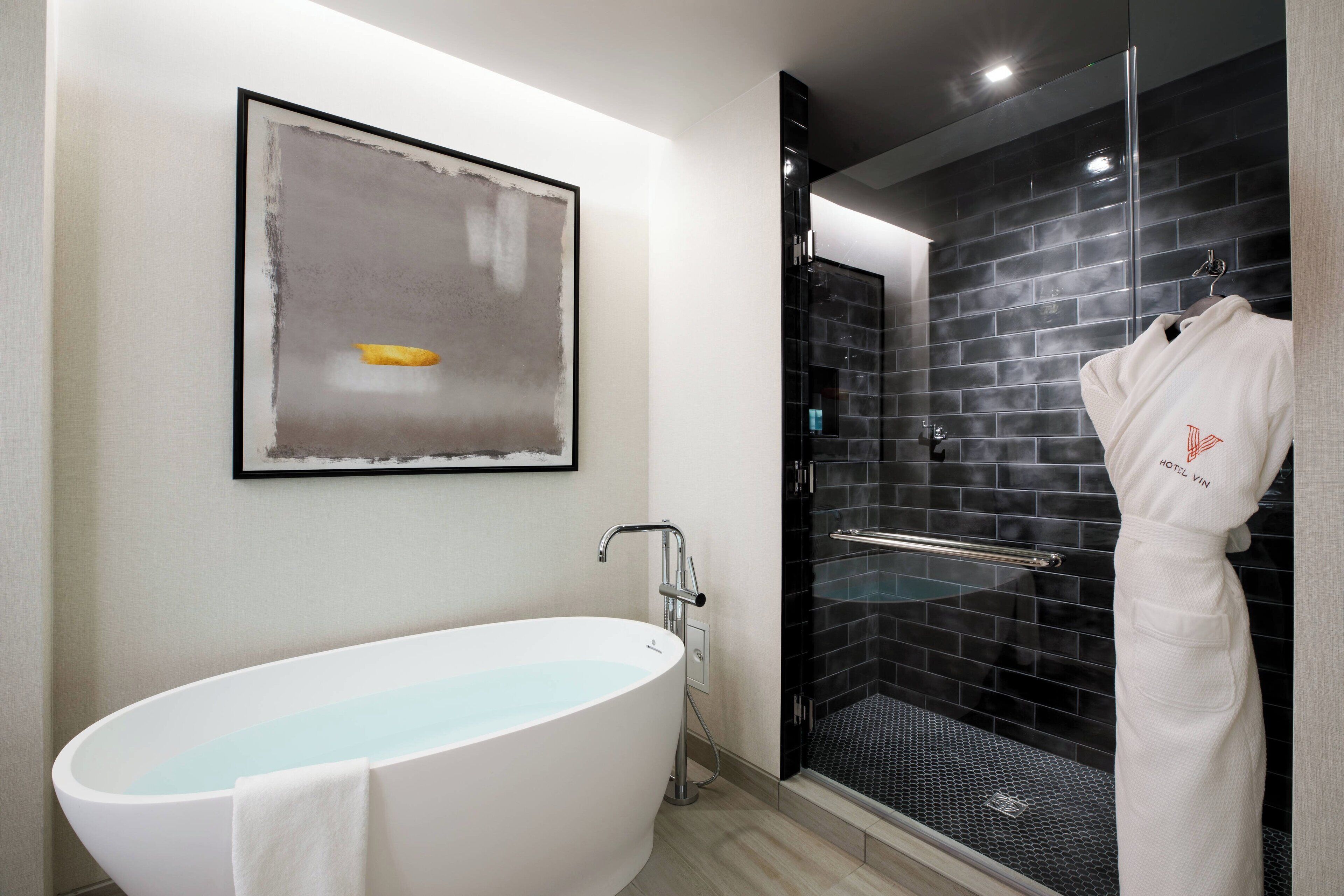 A modern bathroom with a freestanding bathtub, a glass-enclosed shower, and a framed abstract painting on the wall.