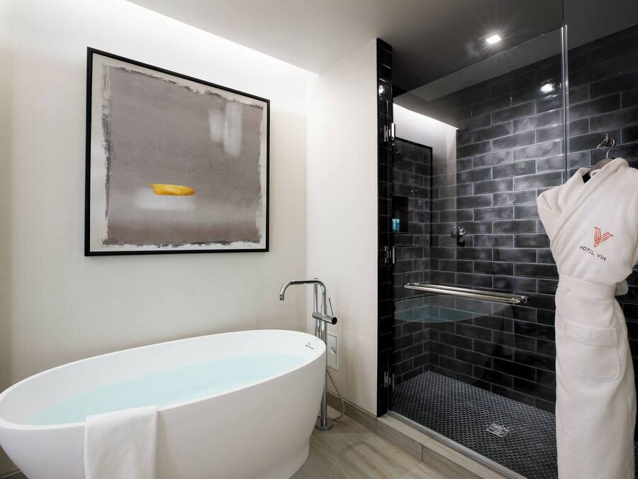 A modern bathroom with a freestanding bathtub, a glass-enclosed shower, and a framed abstract painting on the wall.