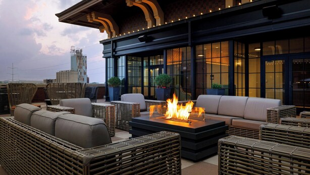 An outdoor seating area with wicker furniture and a central fire feature. - Hotel Vin, Grapevine, Autograph Collection (Grapevine)