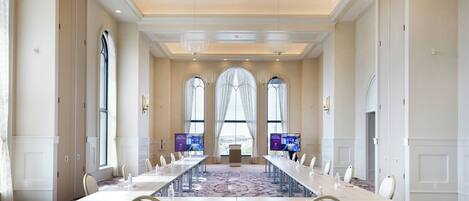 A conference room with a long table, chairs, large windows, and a carpeted floor.