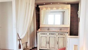A bedroom with a bed, patterned bedding, a wooden cabinet, and a window with curtains. - Provençale charming house  (Mougins)