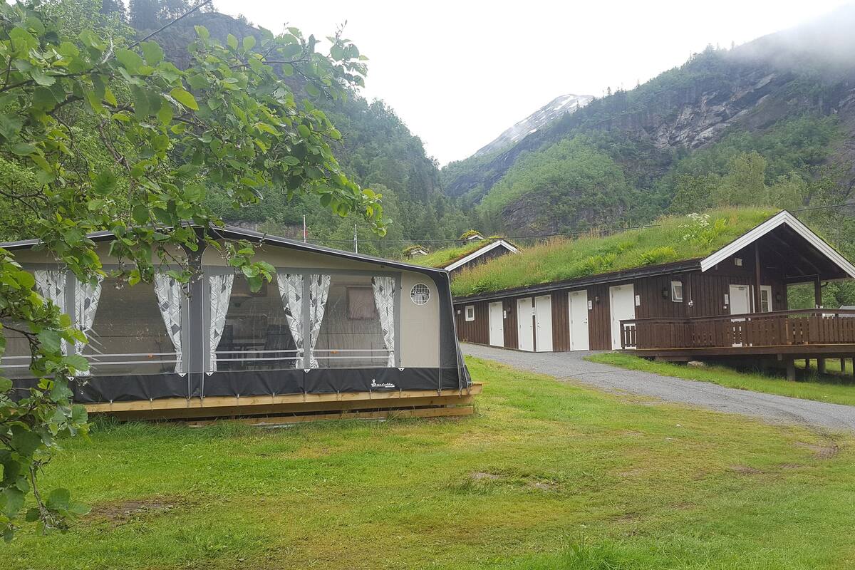 Eine Reihe von Holzhütten mit einem grasbewachsen Weg, der zu ihnen führt, vor einer Bergkulisse.