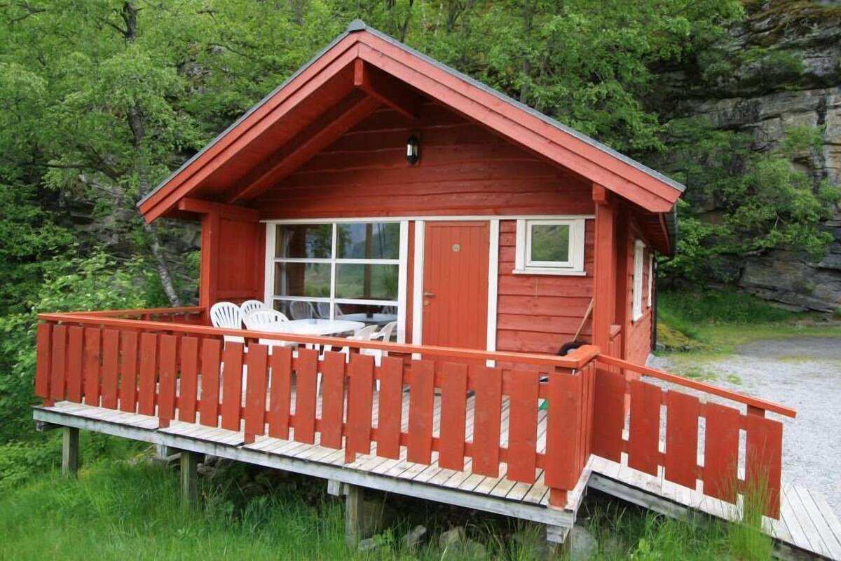 Eine kleine, rote Holzhütte mit einer Terrasse und einem Fenster.