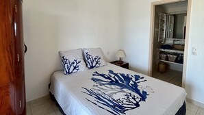 Een slaapkamer met een bed, een houten kledingkast en een badkamer zichtbaar door een geopende deur.