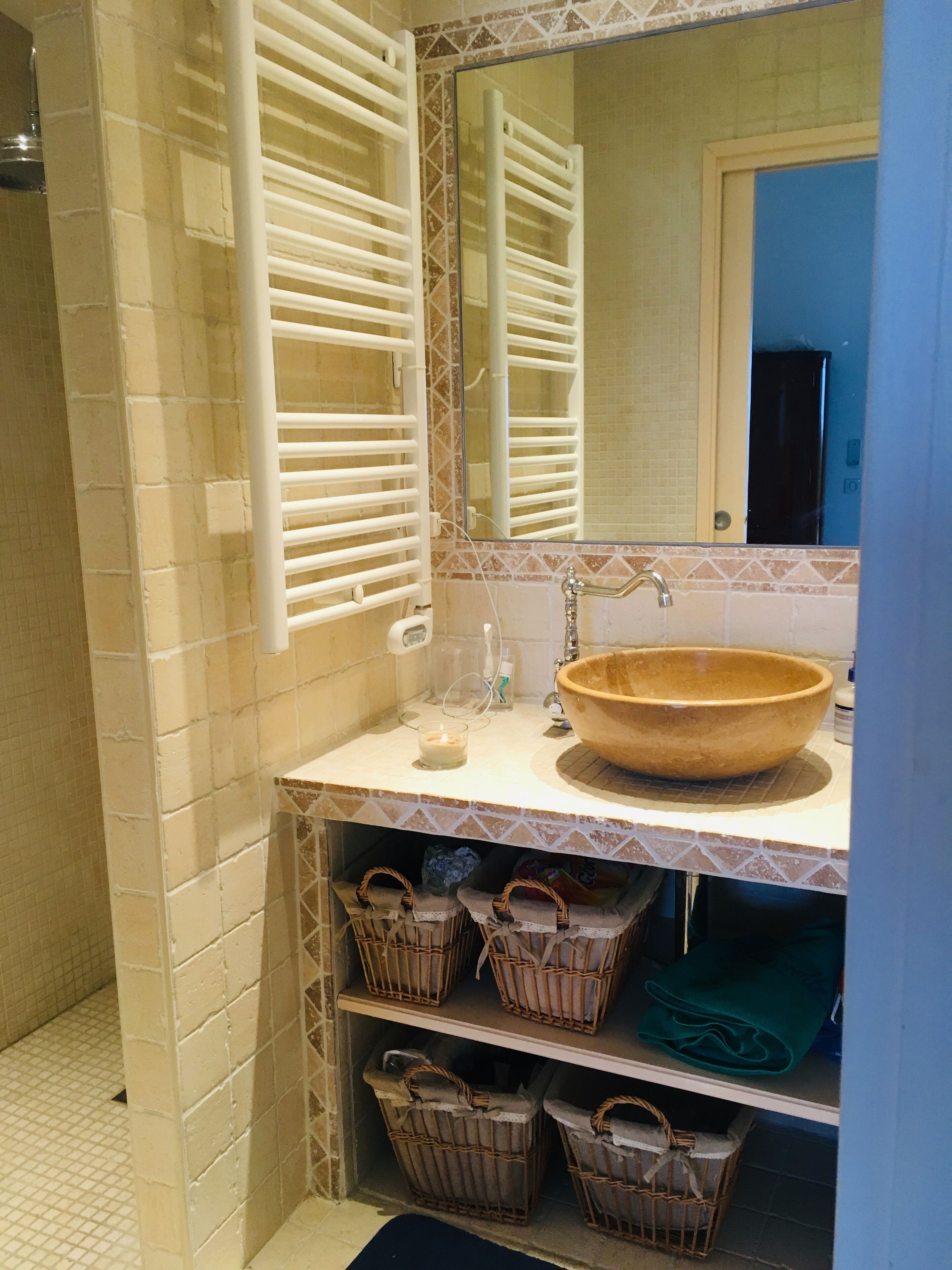 A bathroom with a large mirror, a wooden bowl sink, and wicker baskets on shelves.