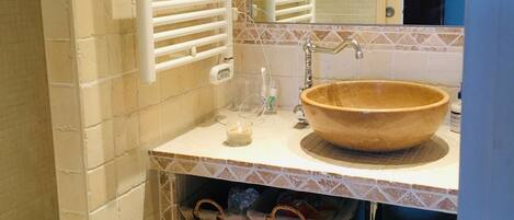 A bathroom with a large mirror, a wooden bowl sink, and wicker baskets on shelves.