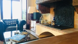 Een woonkamer met een open haard, een leren bank, een bijzettafeltje met boeken en een televisie.