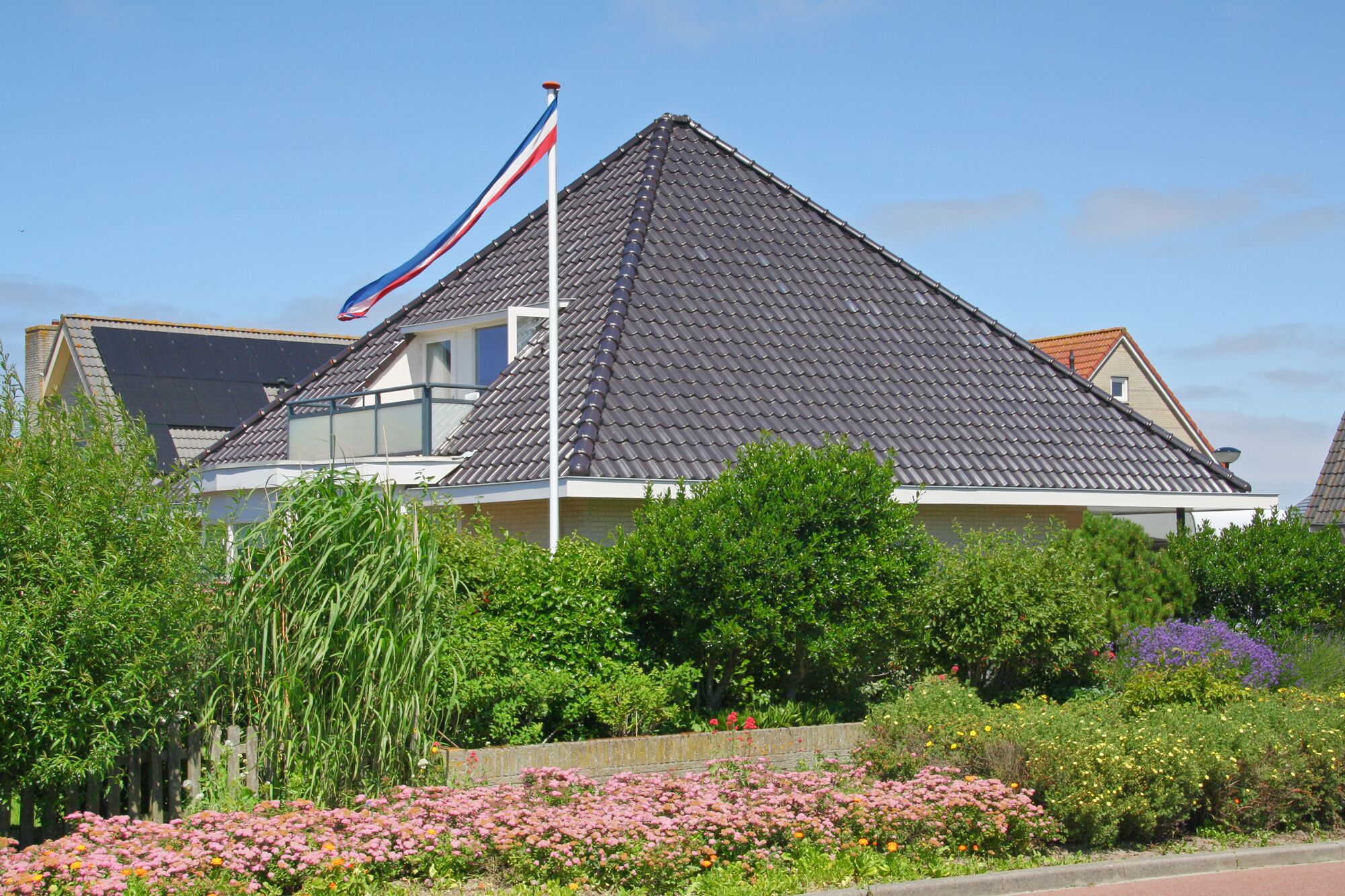 A house with a steeply pitched roof, surrounded by lush greenery and flowering plants.