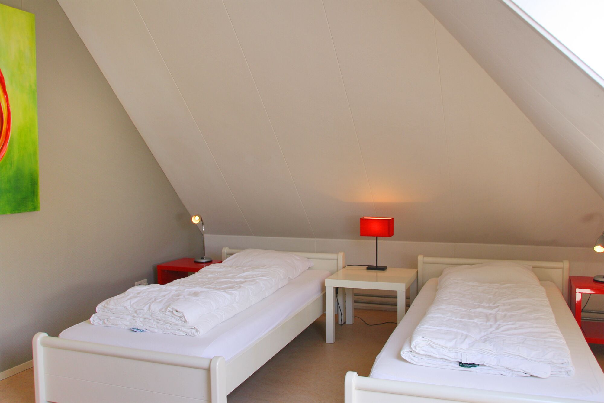A small, triangular attic bedroom with two single beds, a small table, and two bedside lamps.