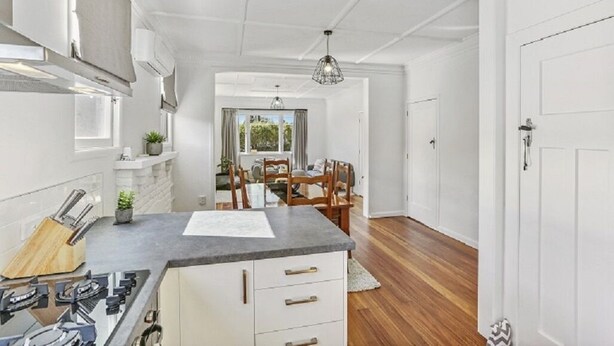 A modern kitchen with white cabinetry, a granite countertop, and a dining area with a wooden table and chairs. - Last Minute Deals - Gisborne Central Location (Inner Kaiti)