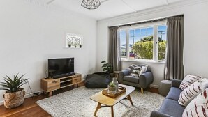A modern living room with a flat-screen TV, grey sofa, and a large window with curtains. - Last Minute Deals - Gisborne Central Location (Inner Kaiti)