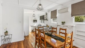 A dining area with a wooden table and chairs, a hanging light fixture, and a kitchen in the background. - Last Minute Deals - Gisborne Central Location (Inner Kaiti)