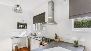 A modern kitchen with white cabinets, a stainless steel range hood, a gas stove, and a window providing natural light. - Last Minute Deals - Gisborne Central Location (Inner Kaiti)