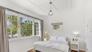 A bedroom with a bed, bedside tables, a hanging light fixture, and a window with curtains. - Last Minute Deals - Gisborne Central Location (Inner Kaiti)