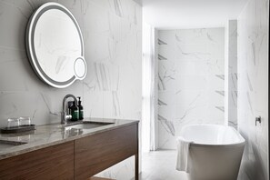 Une salle de bain moderne avec un pare-baignoire en marbre, une baignoire sur pieds et un meuble-lavabo avec un miroir et un évier.