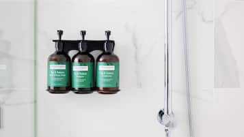 Un baño con tres botellas de jabón de manos y cuerpo, champú y acondicionador Fig & Feijoa en un estante de pared.