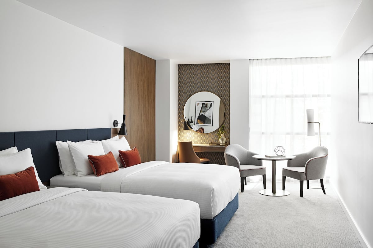 Een hotelkamer met twee bedden, een bureau, twee stoelen, een ronde tafel en een grote spiegel.
