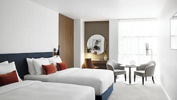 A hotel room with two beds, a desk, two chairs, a round table, and a large mirror.