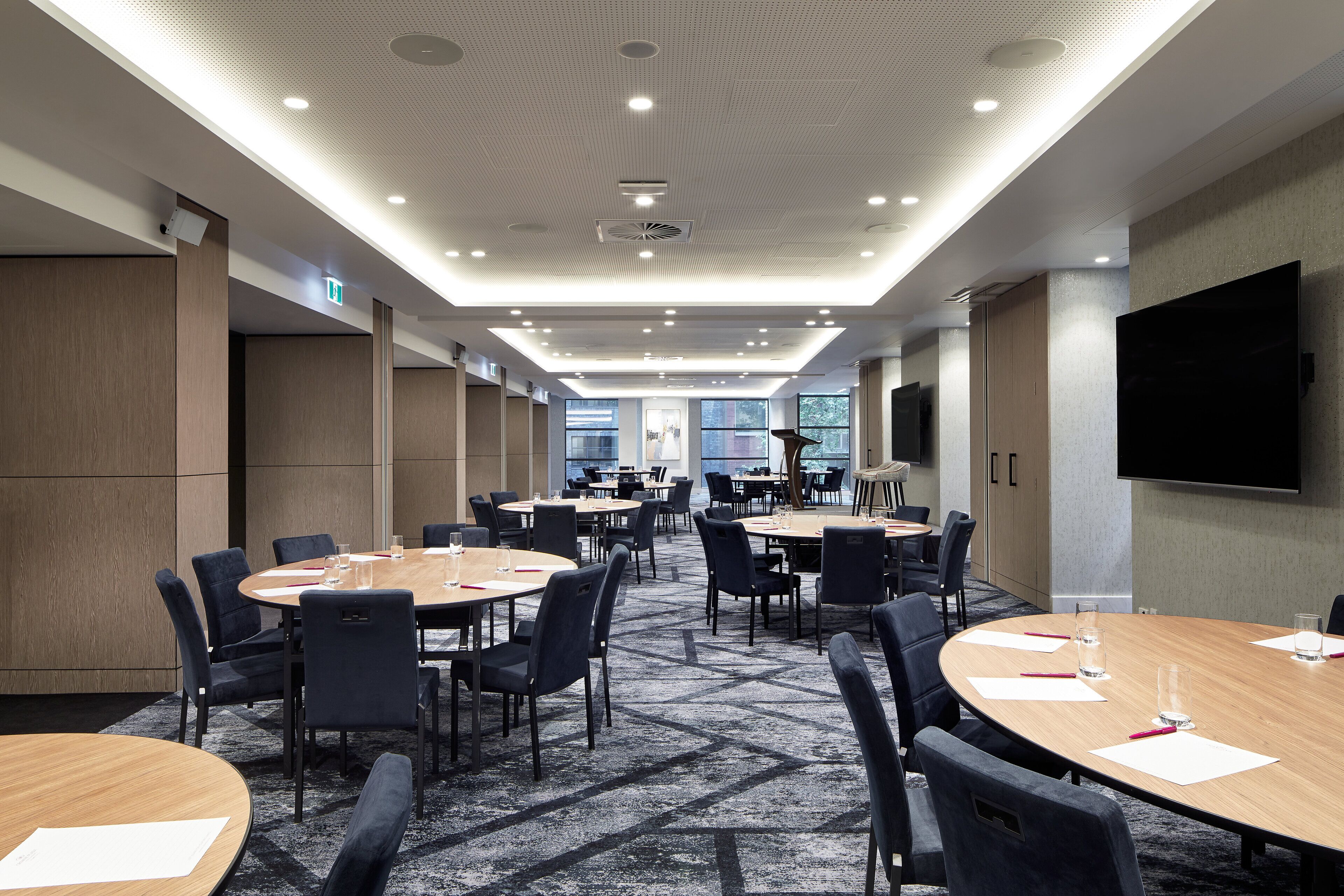 A conference room with round tables, chairs, and a large flat-screen TV on the wall.