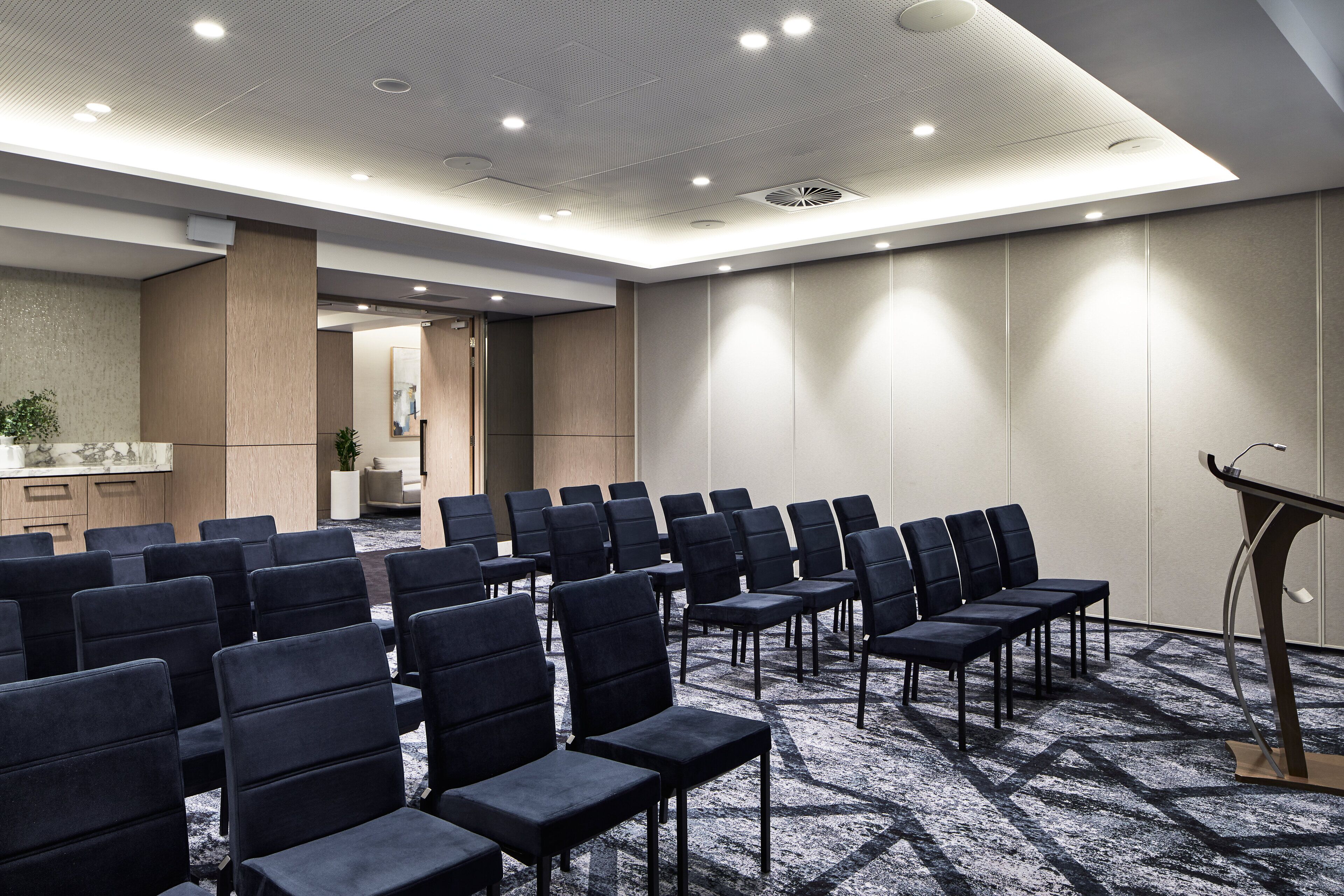 A conference room with rows of chairs, a podium, and a carpeted floor.