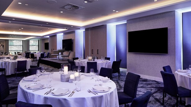 A conference room with round tables set for a meeting, equipped with chairs and a large screen.