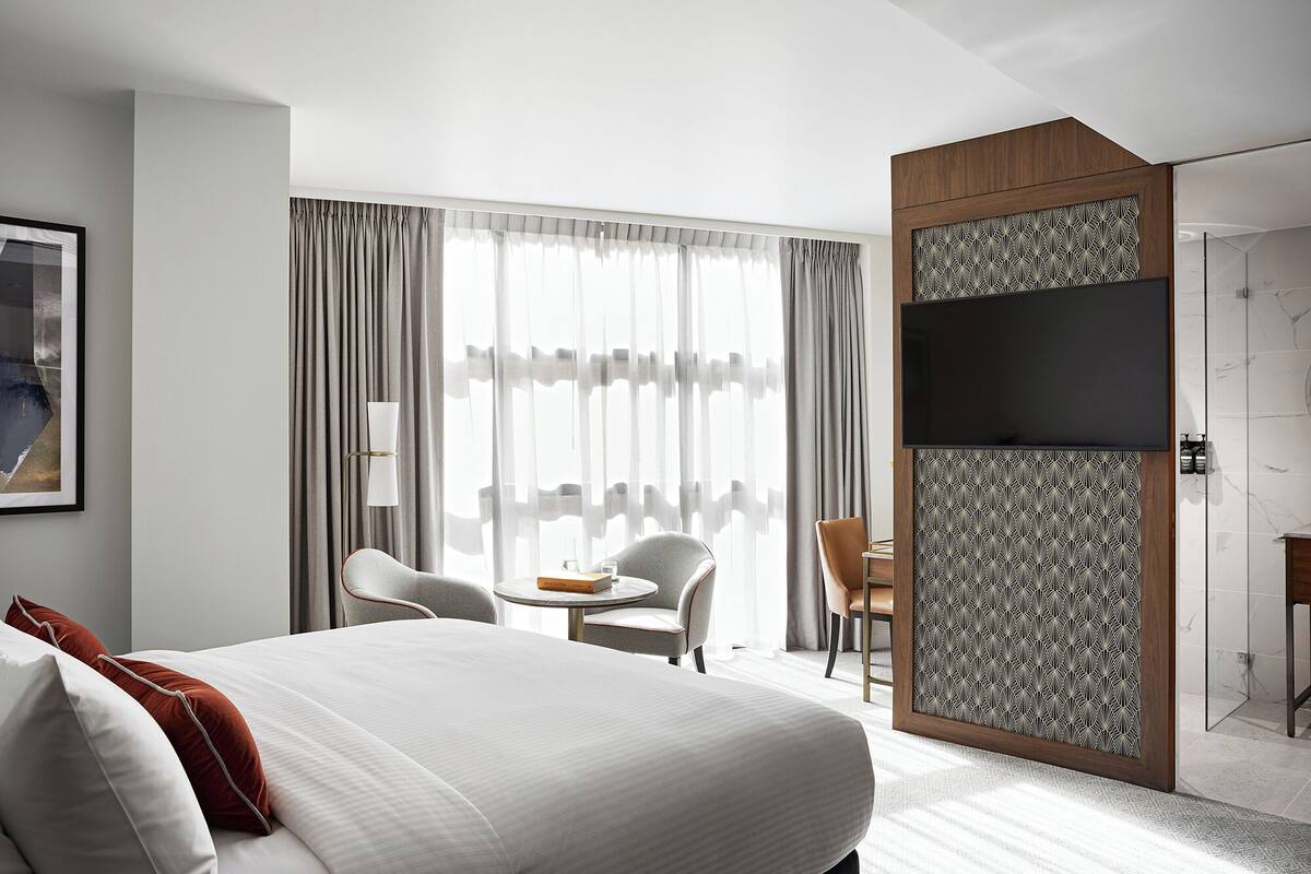 Een hotelkamer met een groot bed, twee stoelen, een tafeltje en een televisie.