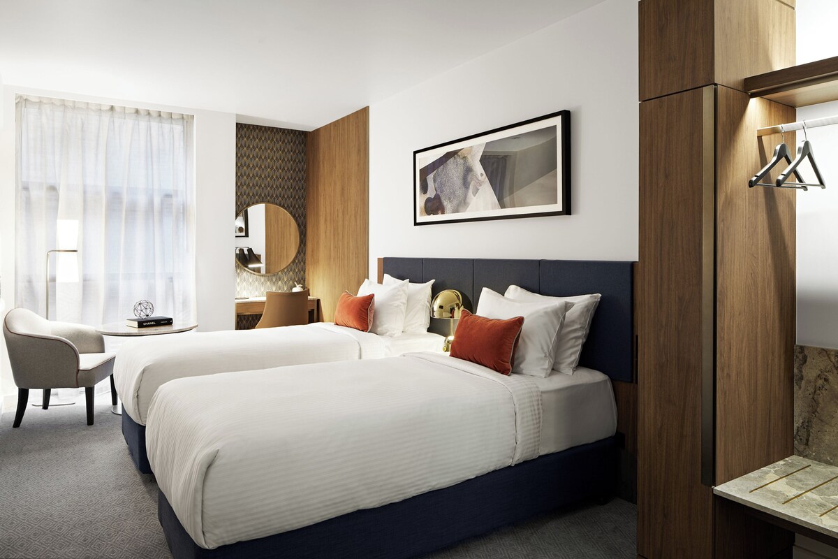 Hotelkamer met twee bedden, een bureau, een stoel, een spiegel en een lijst aan de muur.