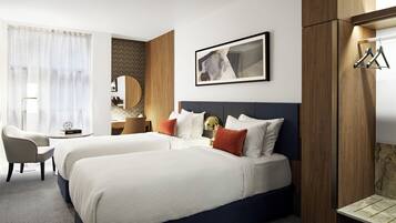A hotel room with two beds, a desk, a chair, a mirror, and a framed picture on the wall.
