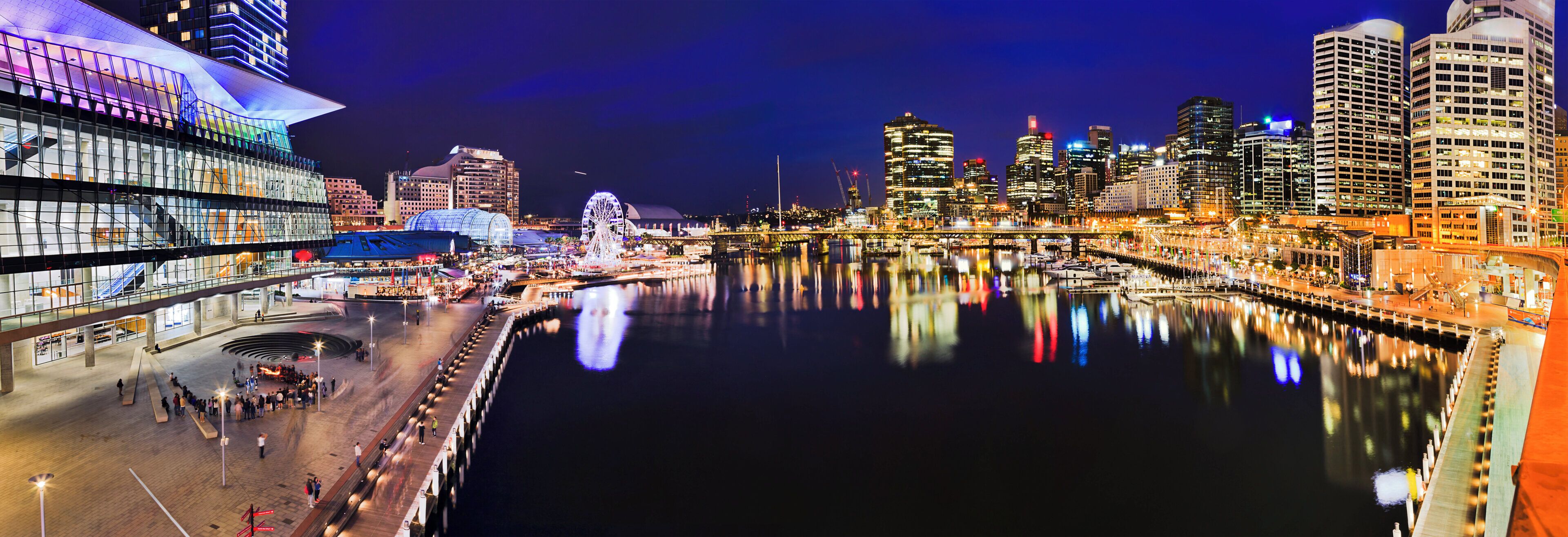 A waterfront cityscape with modern buildings, a bridge, and a waterfront promenade.