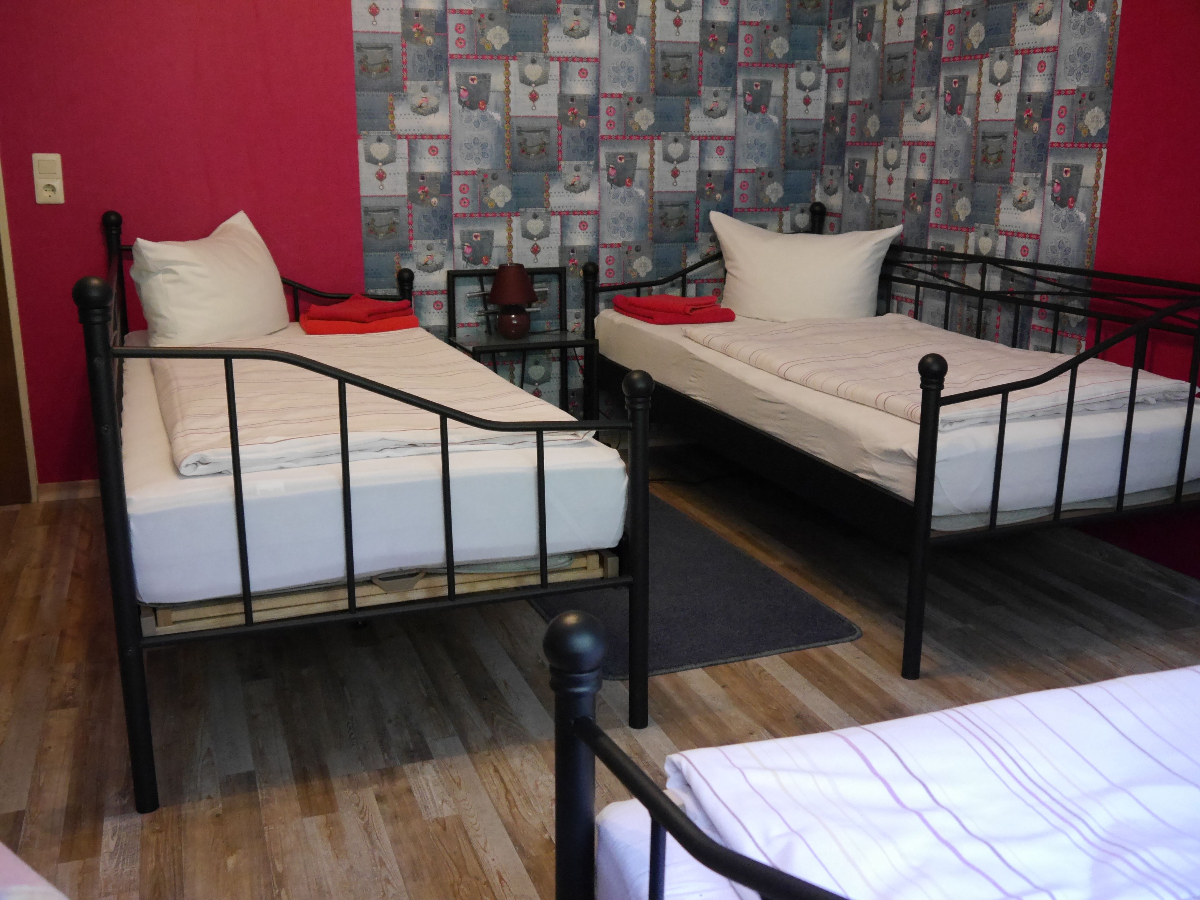Two single beds with metal frames, a red wall, and a patterned wallpaper.