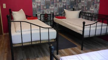 Two single beds with metal frames, a red wall, and a patterned wallpaper.