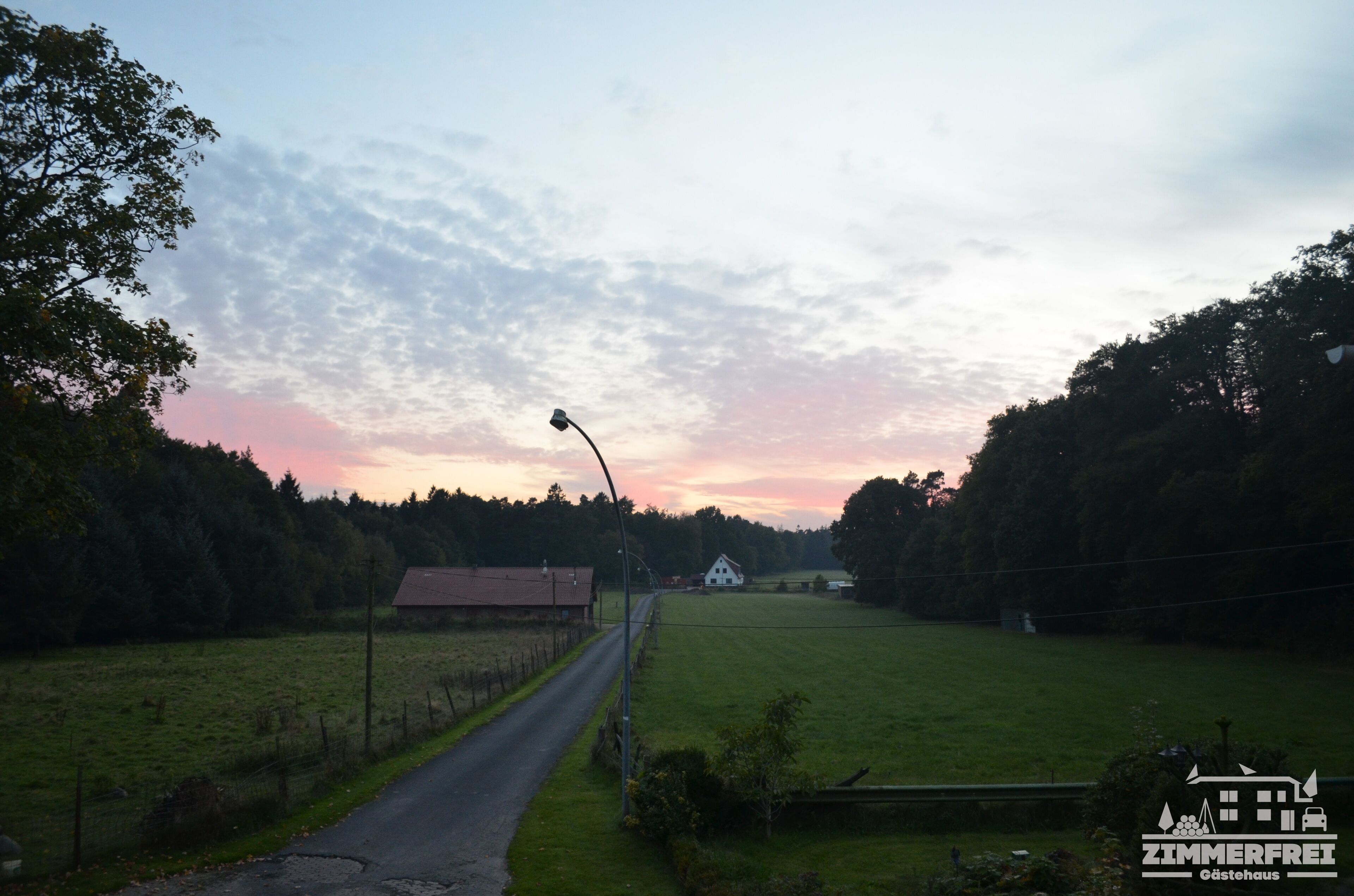 Un paysage rural avec une route, une maison blanche et un champ.