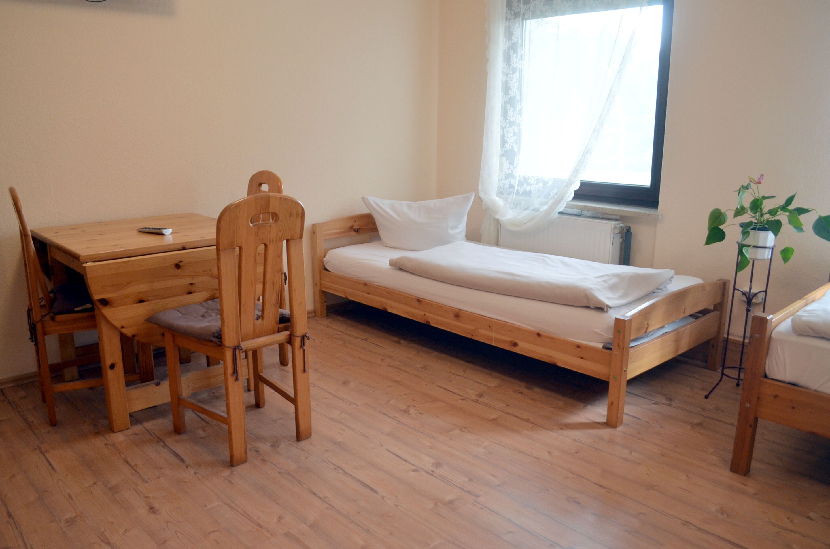 A small, single-room accommodation with a wooden bed, a desk, and a chair.