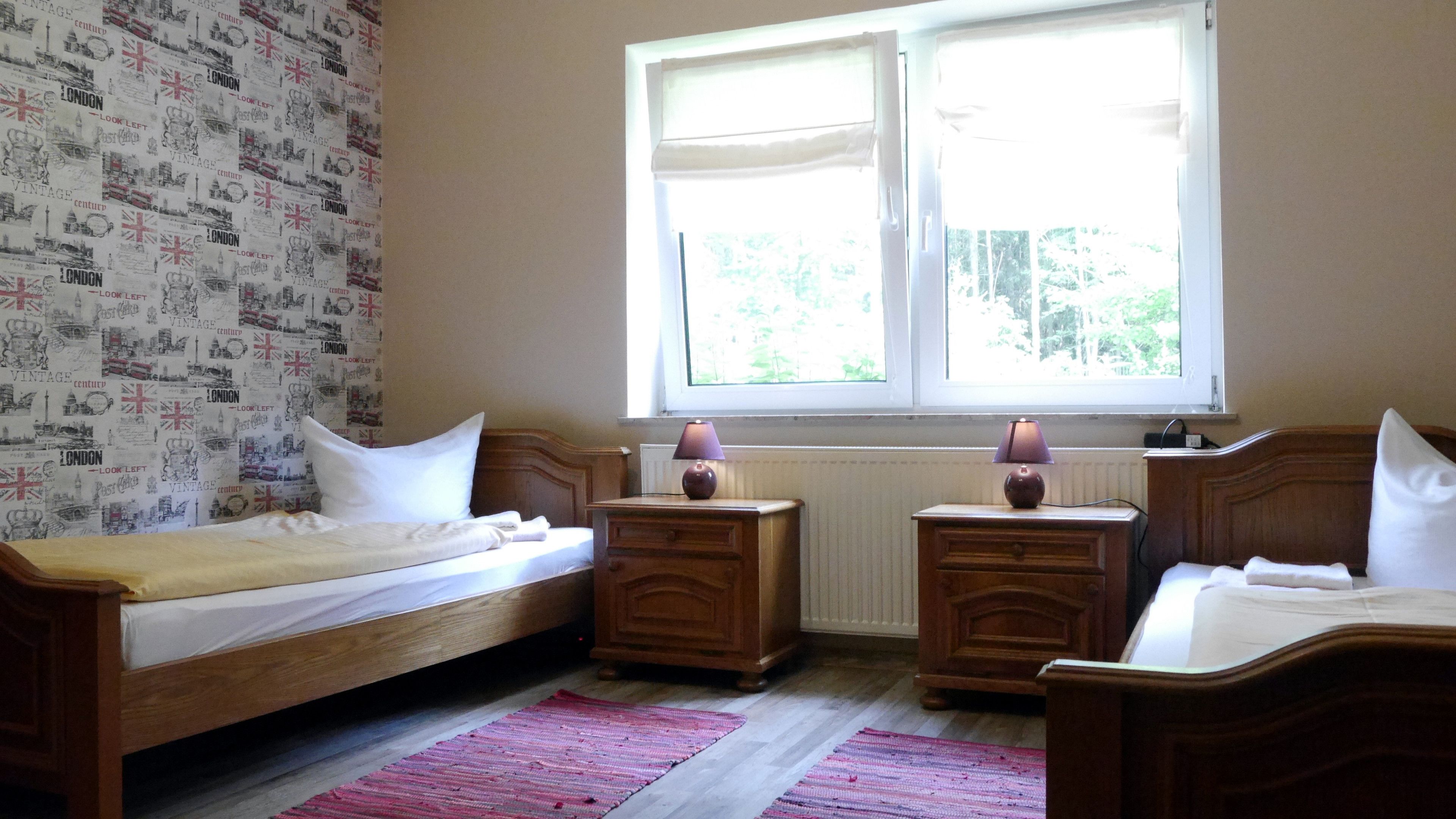 Ein Schlafzimmer mit zwei Einzelbetten, einem Fenster mit Jalousien, einem Heizkörper und einer Wand mit Muster.
