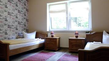 Ein Schlafzimmer mit zwei Einzelbetten, einem Fenster mit Jalousien, einem Heizkörper und einer Wand mit Muster.