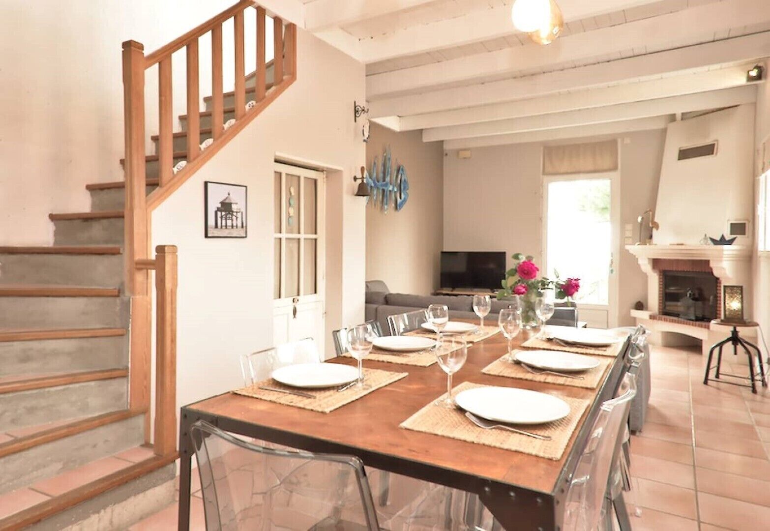 A dining area with a wooden table set for six, a staircase, and a living room with a fireplace.