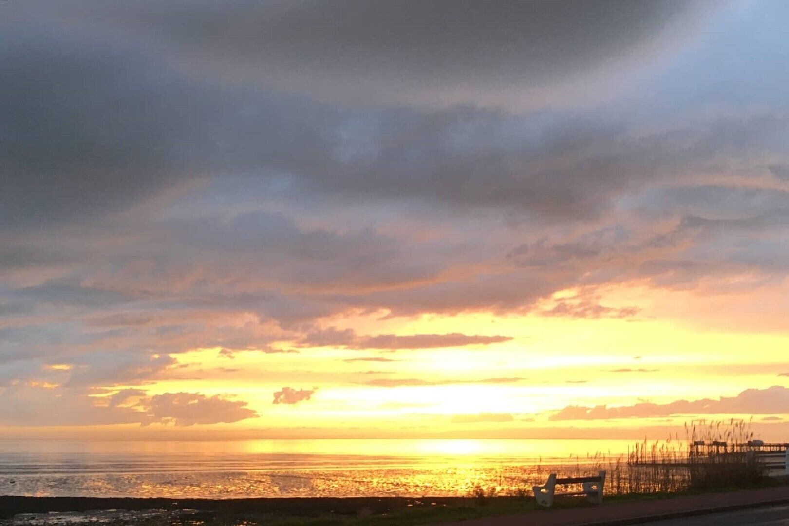 Solnedgang over et kystområde med en vej og vegetation i forgrunden.