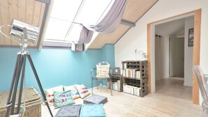 Une pièce avec un plafond en pente, un télescope, une bibliothèque et un lit avec des coussins.