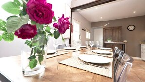 Une table à manger dressée avec de l’argenterie blanche et des verres, un vase rempli de fleurs roses et un plancher en bois.