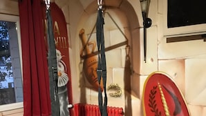 A room with a red curtain, a hanging chair, a shield with a golden emblem, and a wall-mounted lamp. - Chambre Venus (Vichy)