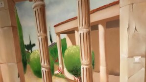 A red cushioned seating area with a mural of a classical building and greenery. - Chambre Venus (Vichy)
