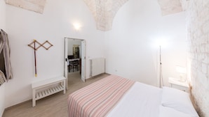 A bedroom with a bed, a bench, a radiator, and a door leading to a dining area. - A casa di Francesca (Ostuni)
