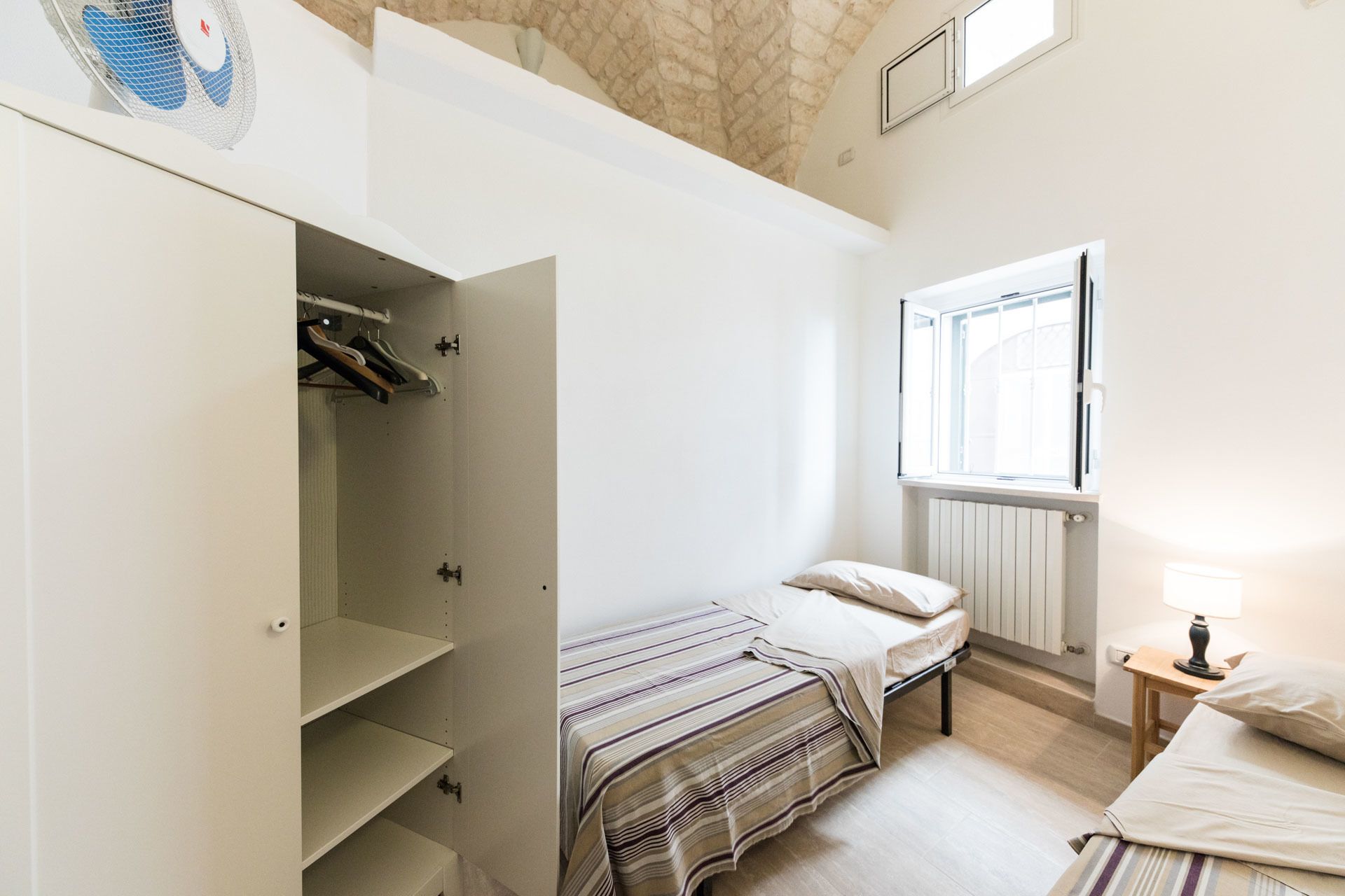 Un dormitorio con cama, armario, radiador y ventana.