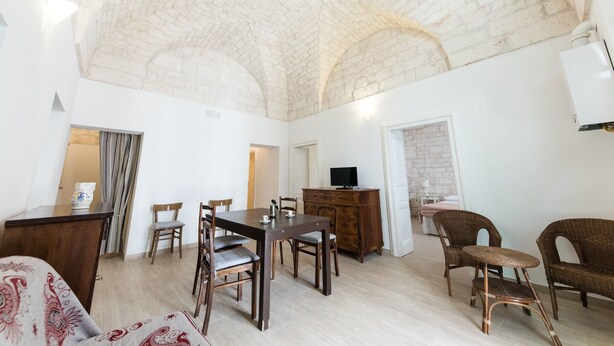 A spacious room with a high arched ceiling, a dining table with chairs, a wooden dresser, and wicker furniture. - A casa di Francesca (Ostuni)