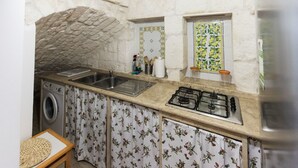A compact kitchen with a stone wall, a washing machine, a gas stove, and a sink. - A casa di Francesca (Ostuni)