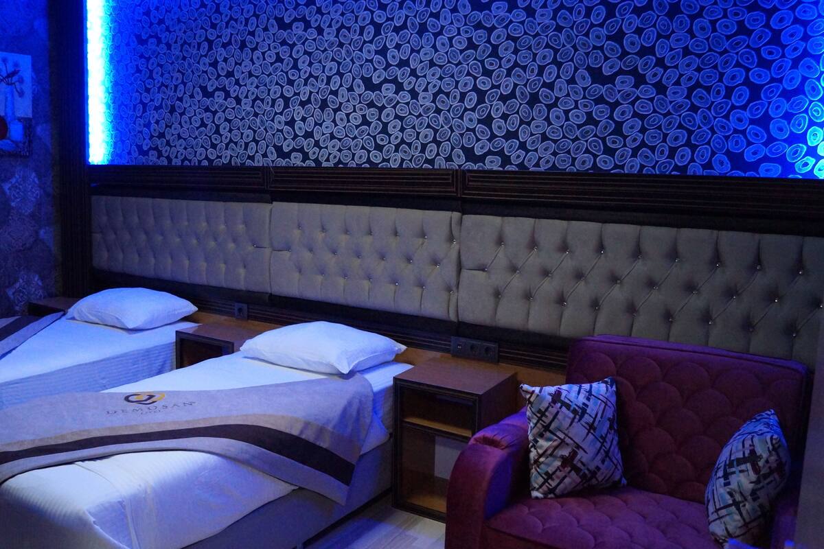 A room with a tufted headboard, two beds with white linens, a red armchair, and a wall with a circular pattern.