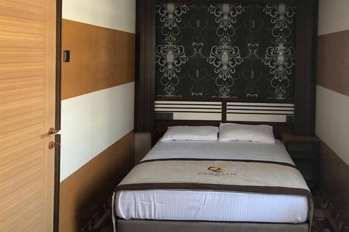 A small, single-bed room with a wooden headboard and a decorative panel above the bed.