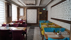 A restaurant with multiple tables and chairs, a brick wall, decorative panels, and an exit sign. - Demosan Hotel Hilden (Hilden)