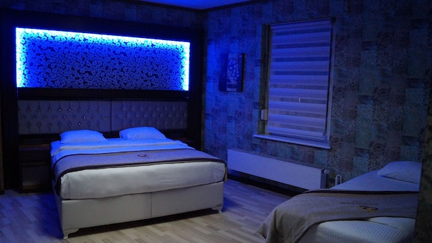 A bedroom with a tufted headboard, a bed with a white mattress, a bedside table, and a wall-mounted light fixture. - Demosan Hotel Hilden (Hilden)
